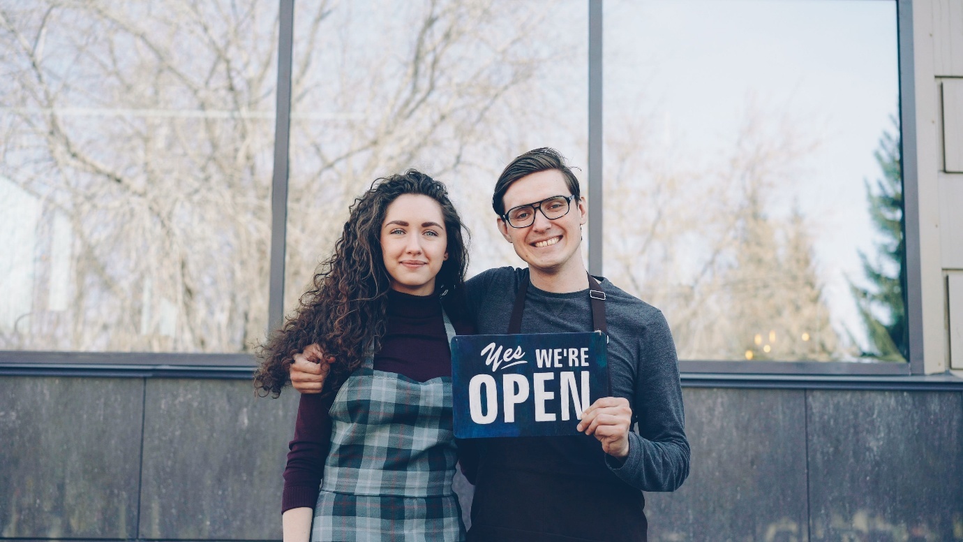 Man and a woman holding a we're open sign